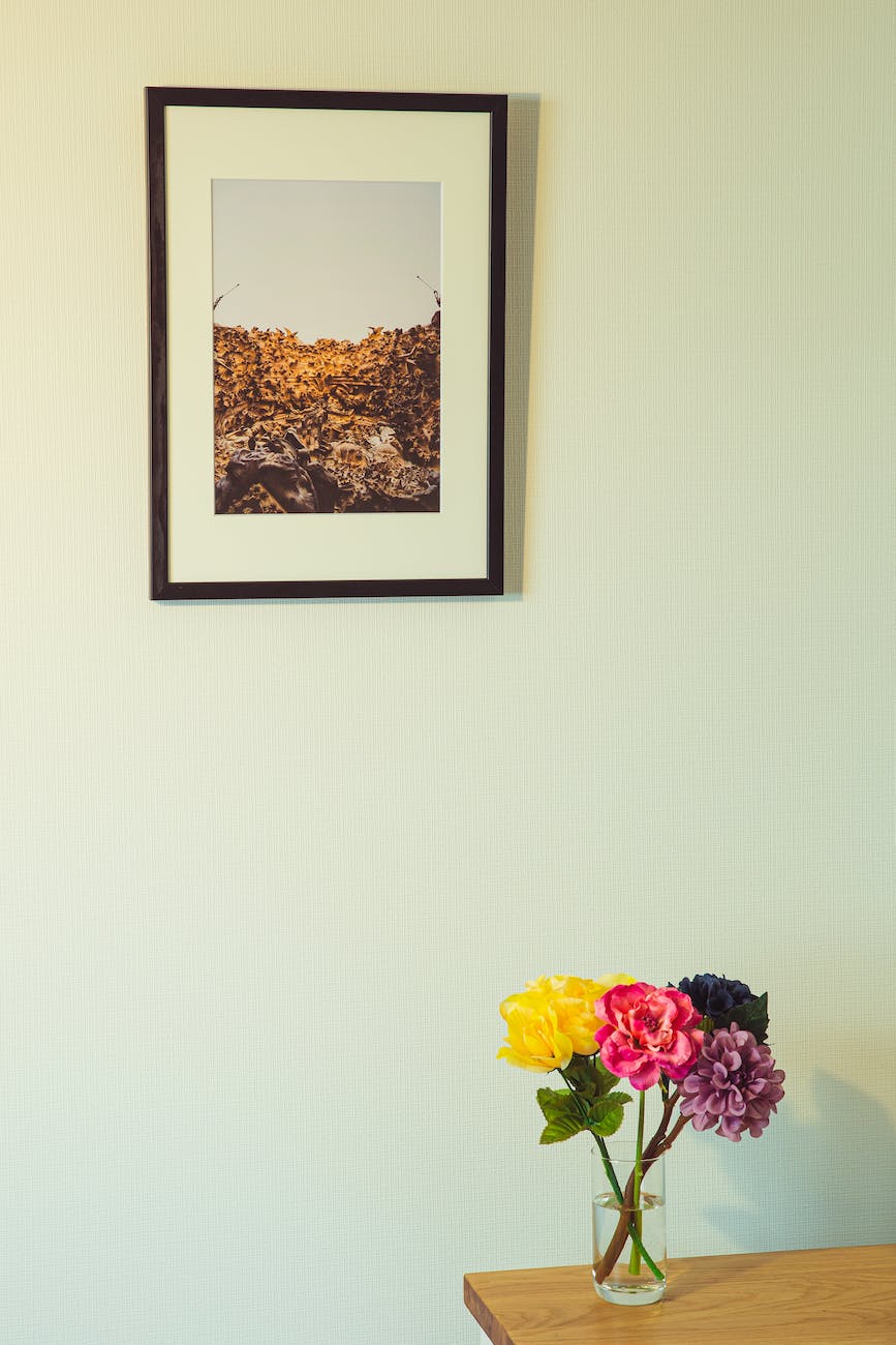colorful flowers in vase on wooden table placed near wall with framed photo
